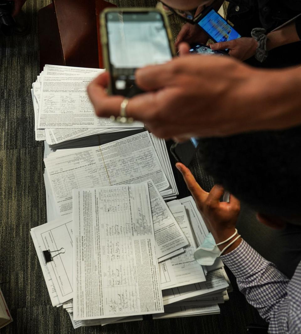 Reporters sift through a stack of fraudulent petitions gathered by a company for Secure MI Vote that are shown during a press conference for Secure MI Vote in downtown Lansing on Wednesday, June 1, 2022.