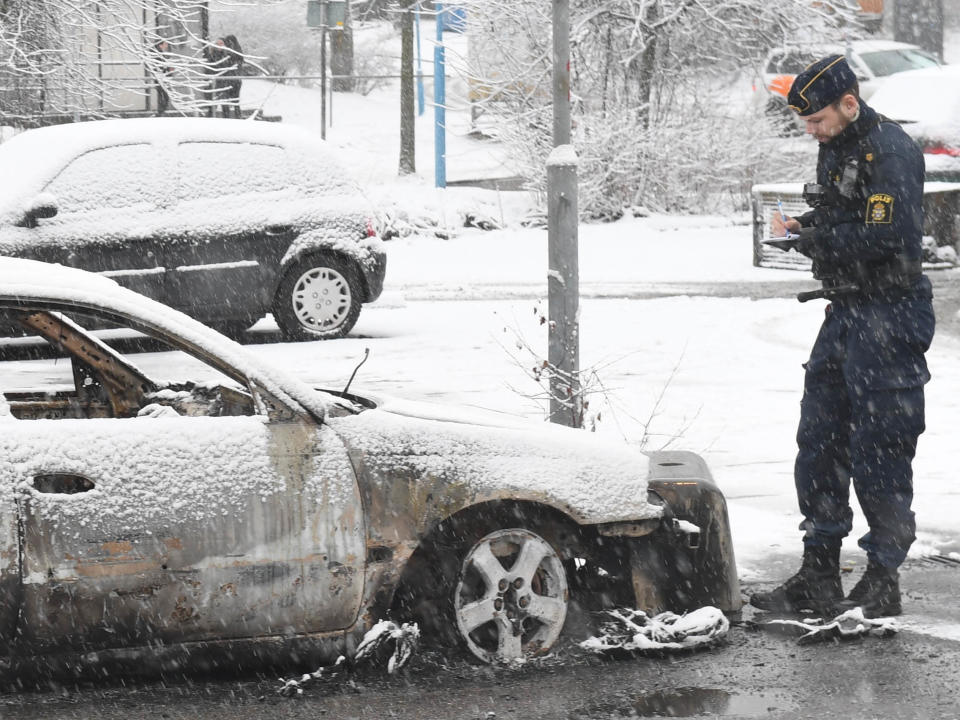 A police officer investigates a burned-out car in the suburb of Rinkeby outside Stockholm: AP