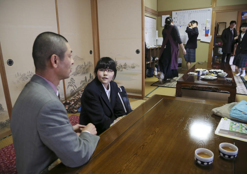 In this Saturday, April 5, 2014 photo, Kokoro Kamiyama, 13, who started her new life after moving from Fukushima, chats with Hiroshi Ueki, a former Fukushima resident, at her dormitory as other female students in school uniform prepare to go to school, in Matsumoto, central Japan. Kamiyama is the first child to sign on to the Matsumoto project which Chernobyl-doctor-turned-mayor Akira Sugenoya of Matsumoto, offered his Japanese town to get children out of Fukushima. Kamiyama was prone to skipping school when she was in Fukushima, which her mother believes was a sign of stress from worrying about radiation. She is happy she can run around outdoors in the city without wearing a mask. “The air feels so clean here,” Kamiyama said. (AP Photo/Koji Sasahara)