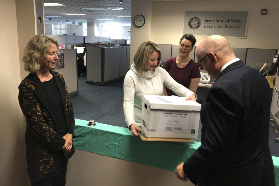 Lydia Plukchi of the Oregon Secretary of State's office in Salem, Ore., accepts on Wednesday, Sept. 18, 2019, a box containing 2,000 signatures backing a proposed ballot measure that would create the most comprehensive law in America requiring the safe storage of weapons, as worker Amanda Kessel, behind her, looks on. Delivering the box are Henry Wessinger, president of the State of Safety Action which is backing the proposed measure, and Rep. Alissa Keny-Guyer. (AP Photo/Andrew Selsky)