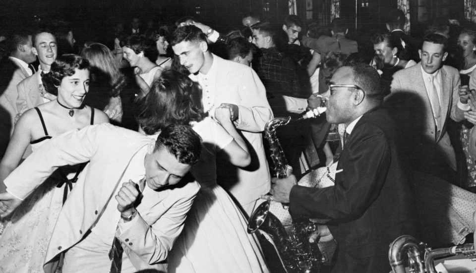 People dance enthusiastically to live saxophone music at a crowded party