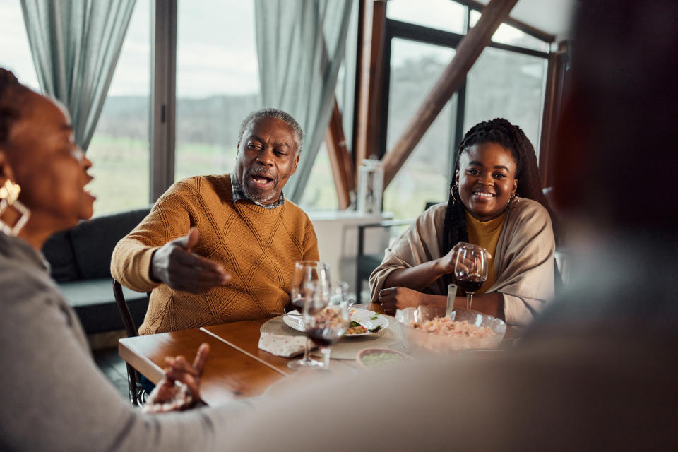 A group of people talking and smiling around a dining table with food and wine glasses in a cozy, well-lit room