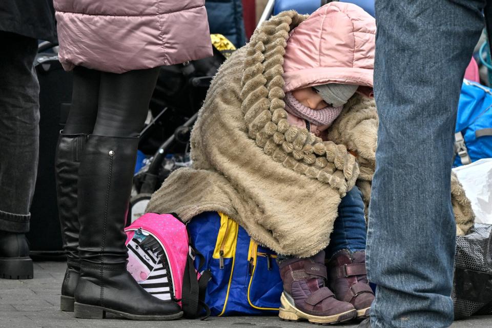 A child wrapped in a blanket sits on luggage while waiting to be relocated from the temporary shelter for refugees in a former shopping center between the Ukrainian border and the Polish city of Przemysl, in Poland