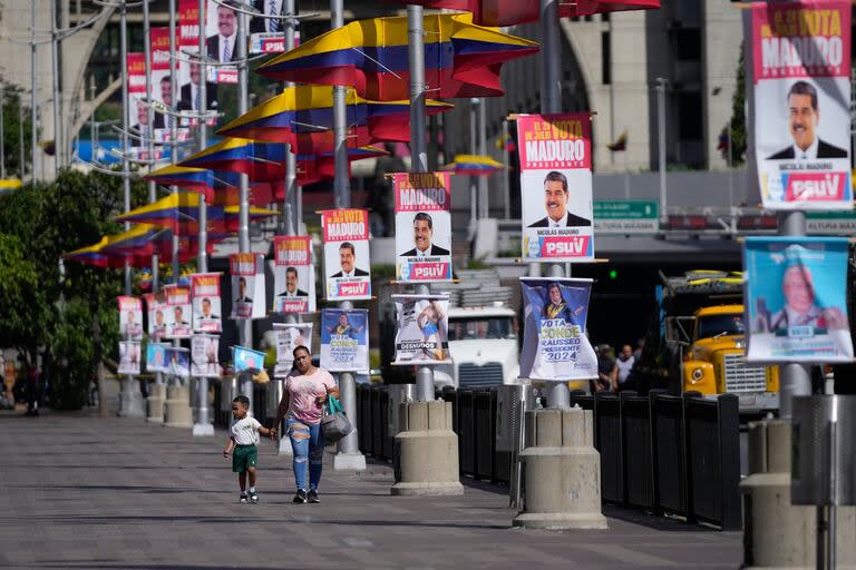 Una mujer y su hijo caminan por una calle llena de carteles de campaña que promocionan al presidente Nicolás Maduro, quien se postula para un tercer mandato, en Caracas, Venezuela