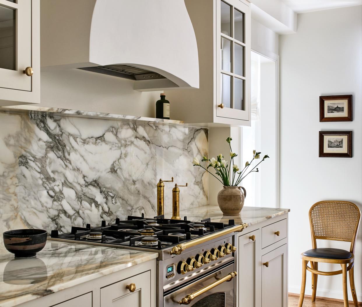  A kitchen with a veined backsplash, antique knobs and a white palette. 