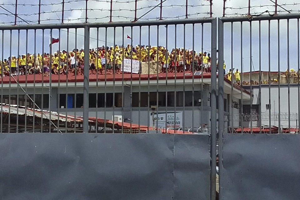 Filipino inmates stand on top of the roof of a prison building as they protest in Pototan town, Iloilo province, central Philippines on Wednesday Aug. 24, 2022. About 100 inmates in an overcrowded jail climbed atop the roof of a prison building in the central Philippines and noisily protested with raised fists and placards, saying they were not being fed well and demanding the removal of the jail warden, who was immediately suspended, jail officials said Thursday. (AP Photo/Fred Pasgala)