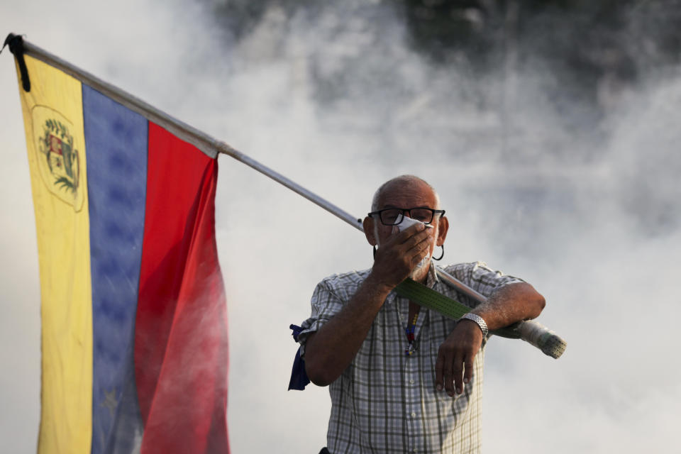 A Maduro opponent carrying a Venezuelan flag covers his face against the tear gas fired during an attempted military uprising to oust the president on April 30, 2019. (Photo: ASSOCIATED PRESS)