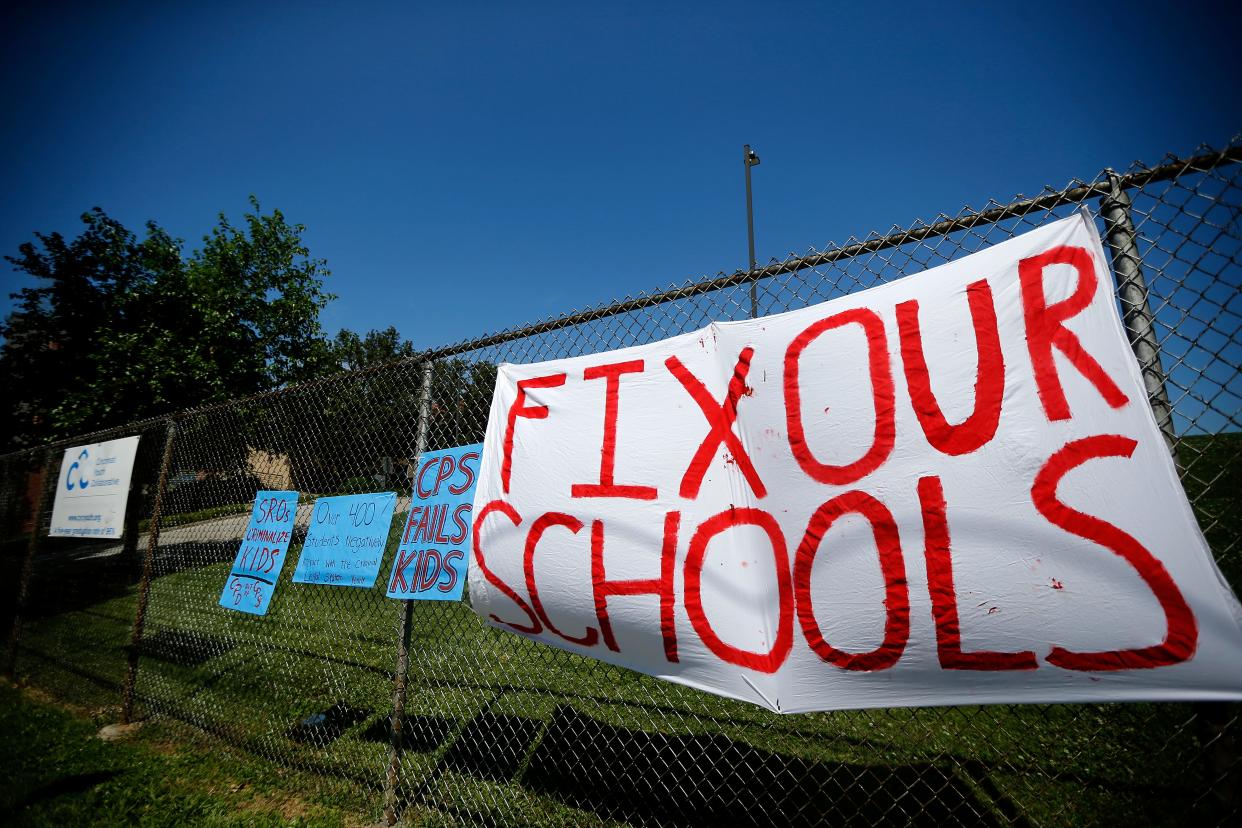 Students from the Young Activists Coalition clip a sign to the fence near the main entrance of the Cincinnati Public Schools administrative building in the Corryville neighborhood of Cincinnati in June 2021.