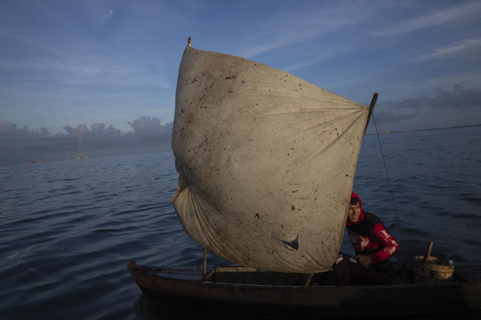 Yohandry Colina uses an oil-stained sheet for a sail on the boat he uses to put fish he catches in Lake Maracaibo in Cabimas, Venezuela, Wednesday, Oct. 12, 2022. (AP Photo/Ariana Cubillos)
