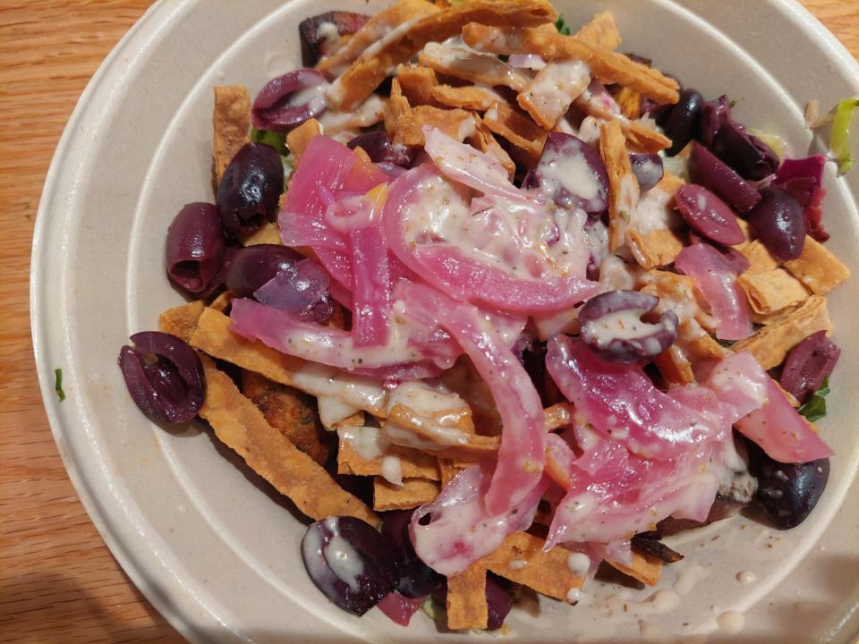 A bowl containing tortilla chips, pink onion, black olives, sauce and salad from the Cava restaurant in Chicago