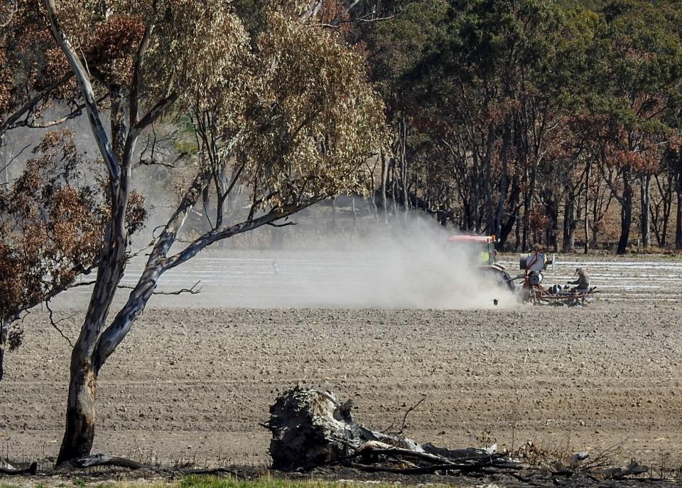 A trail of dust blows behind a tractor in a dry field.