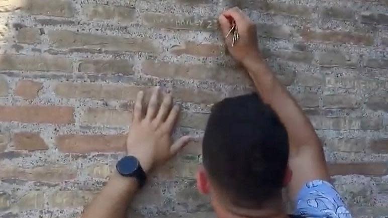 Turista tallando su nombre y el de su novia en la pared del Coliseo Romano