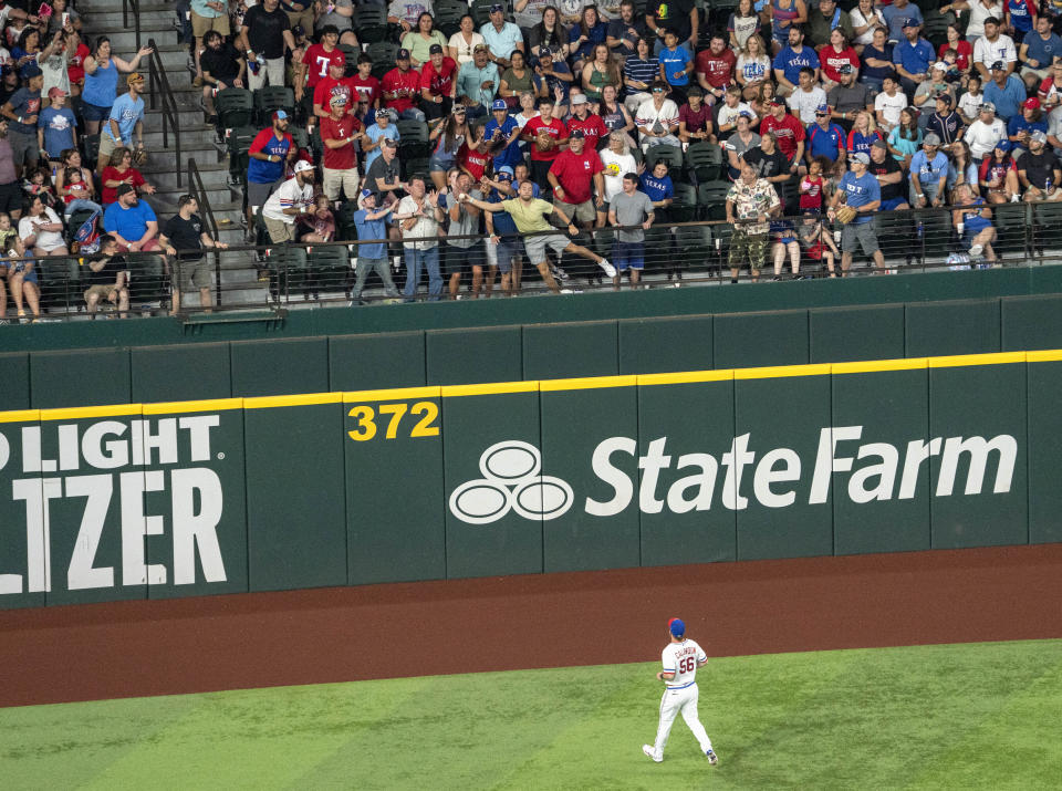 Texas Rangers left fielder Kole Calhoun (56) looks up as fans scramble to catch a two-run home run by Washington Nationals' Nelson Cruz during the sixth inning of a baseball game Saturday, June 25, 2022, in Arlington, Texas. (AP Photo/Jeffrey McWhorter)