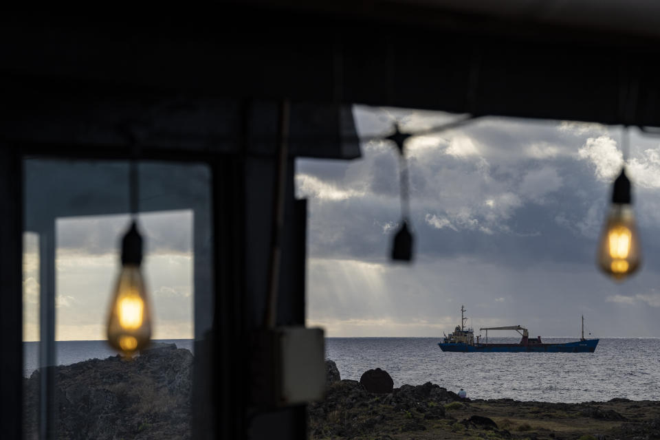 Un barco que abastece a la Isla de Pascua con productos de Chile continental está anclado frente a Hanga Roa, Rapa Nui, visto desde un restaurante, el domingo 27 de noviembre de 2022. La forma más rápida de llegar aquí es un vuelo de seis horas desde Santiago, Chile. (Foto AP/Esteban Félix)