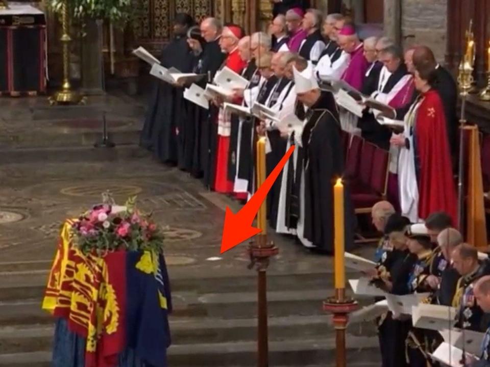 arrow pointing to a piece of paper on the ground near queen Elizabeth's coffin