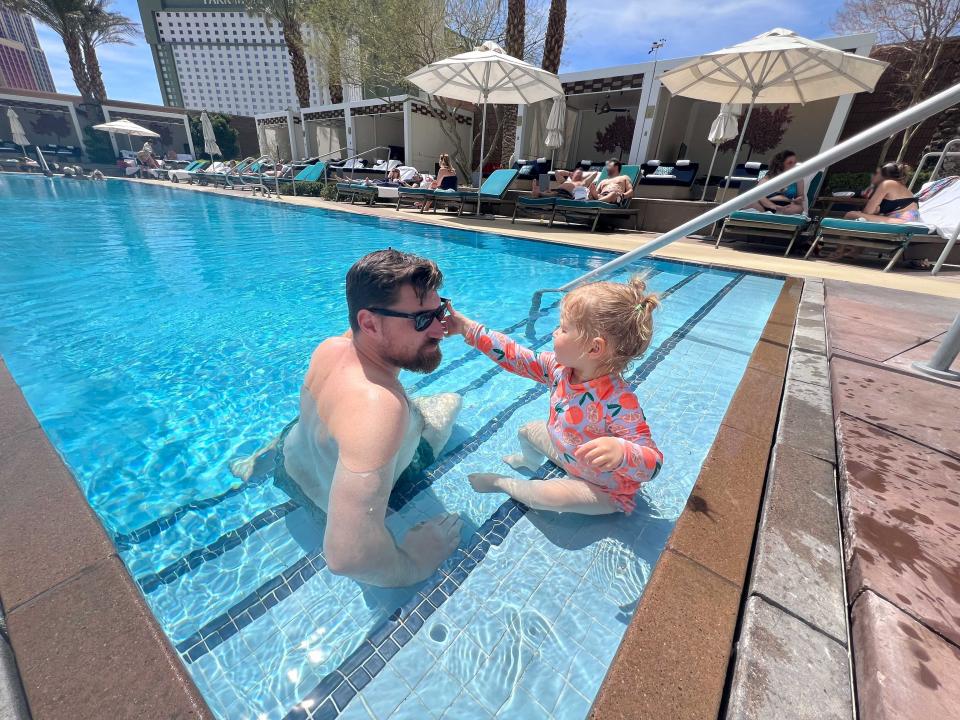 A man and his child sit on the steps inside a pool.