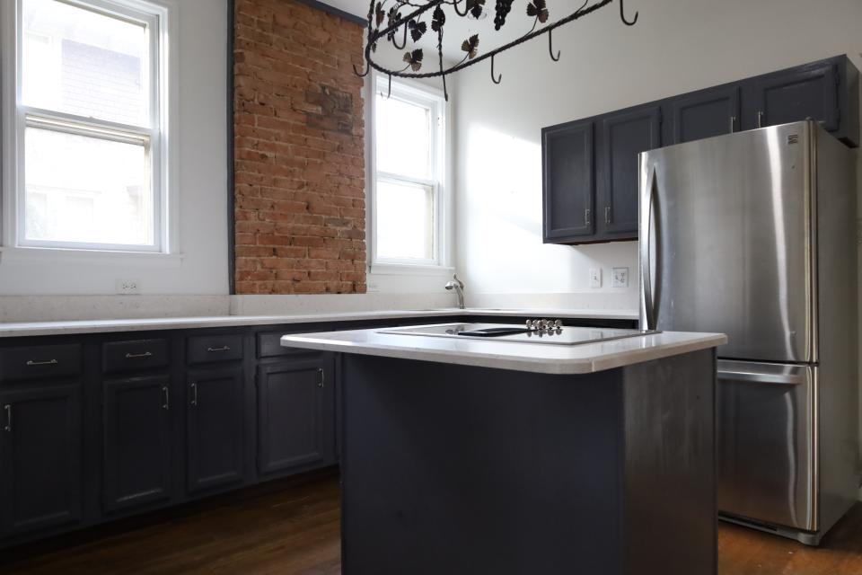 A brand-new kitchen in the Central Gardens home. This modern kitchen in a 100 plus year-old home features a new fridge, island stovetop, new dark grey cabinets and granite countertops which fade into the backsplash.