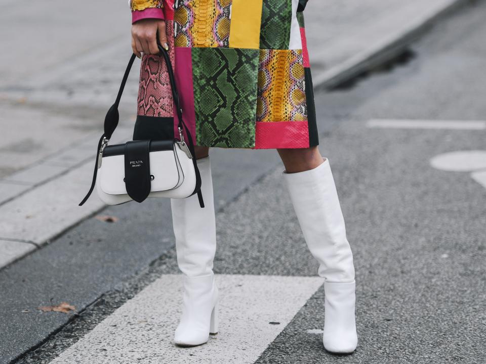 woman wearing white knee high booths with a colorful quilted coat and a black and white bag