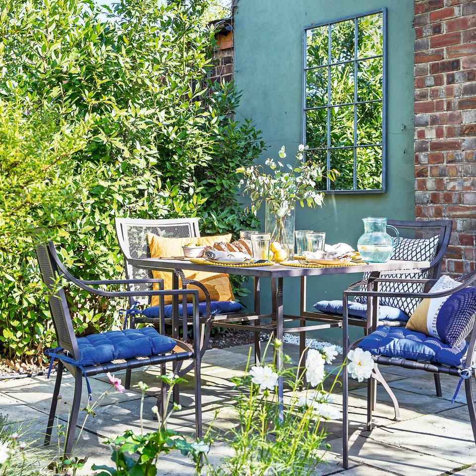 Garden with table and chairs set and garden mirror on brick wall.
