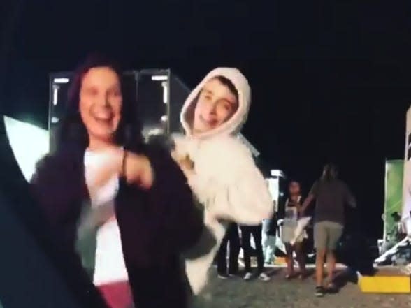 millie bobby browna dn noah schnapp, seen through the open door of a car, laughing and dancing while wearing hoodies