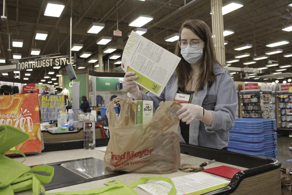 Sara Plush, an employee of the grocery chain Fred Meyer, adds a sheet with information about how to get a COVID-19 vaccine to groceries ordered by a homebound senior citizen in Portland, Ore., through the nonprofit group Store to Door on Feb. 25, 2021. An untold number of older people are getting left behind in the desperate dash for shots because they are too frail, overwhelmed, isolated or poor to navigate a system that favors healthier individuals with more resources. Nonprofits, churches and health care outreach workers are scrambling to to reach older people who are falling through the cracks before the nation’s focus moves on and the competition for vaccines stiffens. (AP Photo/Gillian Flaccus)