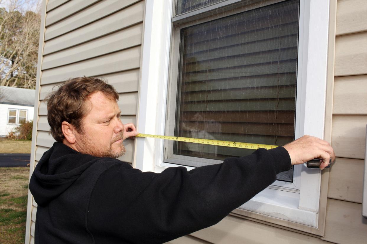 man, with a tape measure, measuring the width of a window on the exterior of a house