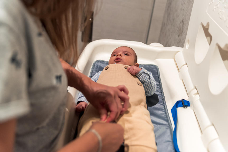 Baby on changing table with adult securing them in overalls, depicting infant care