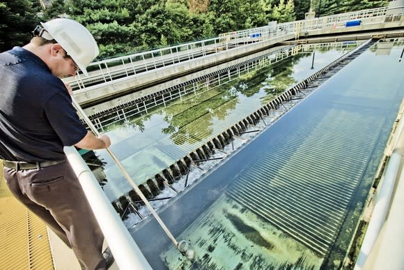 Worker with hard hat probing a water treatment plant collection pool.