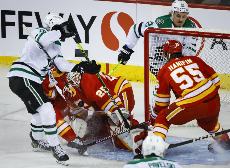 Dallas Stars forward Jason Robertson, left, tries to deflect the puck past Calgary Flames goalie Jacob Markstrom, center, as forward Roope Hintz watches during the first period of an NHL hockey game Saturday, March 18. 2023, in Calgary, Alberta. (Jeff McIntosh/The Canadian Press via AP)