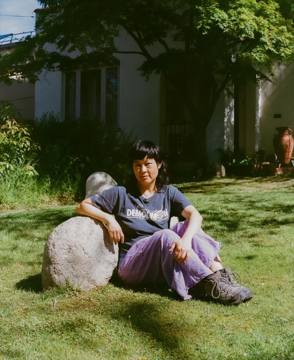 The artist seated against a rock in a garden.