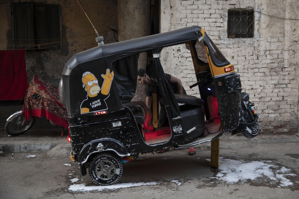 In this Nov. 19, 2019 photo, a tuk-tuk driver washes his vehicle in an alleyway of a slum in Cairo, Egypt. Motorized rickshaws known as tuk-tuks have ruled the streets of Cairo’s slums for the past two decades hauling millions of Egyptians home every day. Now the government is taking its most ambitious stand yet against the polluting three-wheeled vehicles: to modernize the neglected transport system, it plans to replace tuk-tuks with clean-running minivans. (AP Photo/Nariman El-Mofty)