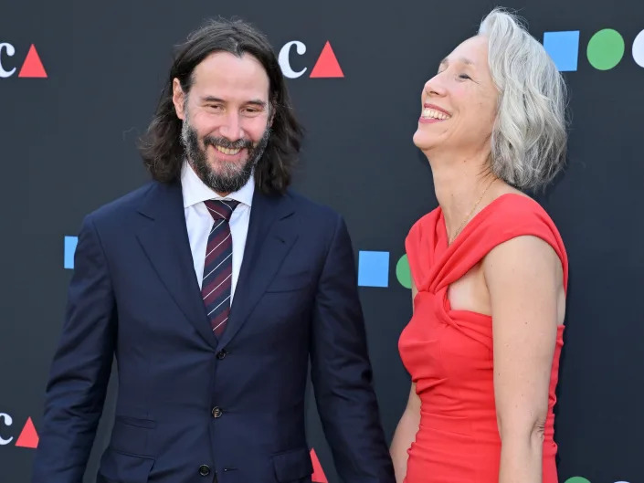 Keanu Reeves and girlfriend Alexandra Grant hold hands while walking the red carpet together.