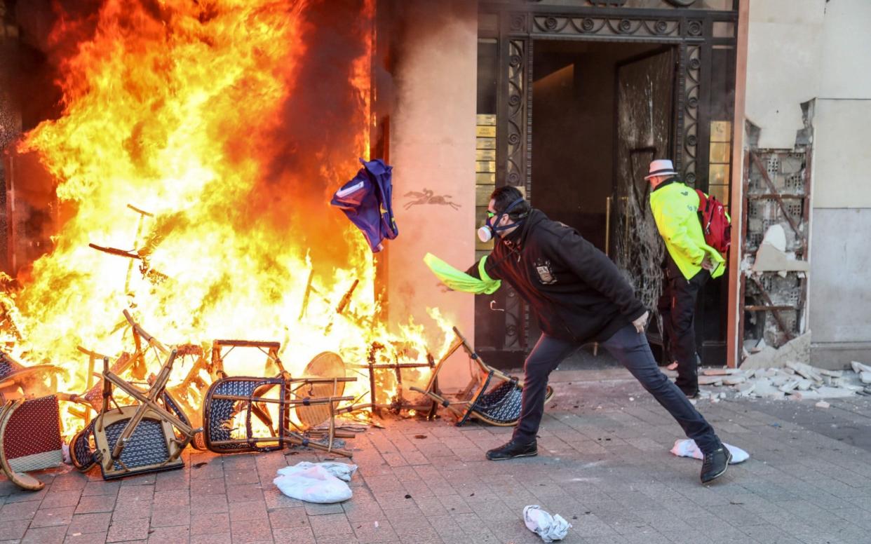 A Yellow Vest protester throws a flag of Europe towards a barricade burning in front of a shop on the Champs-Elysees avenue in Paris on March 16 - AFP