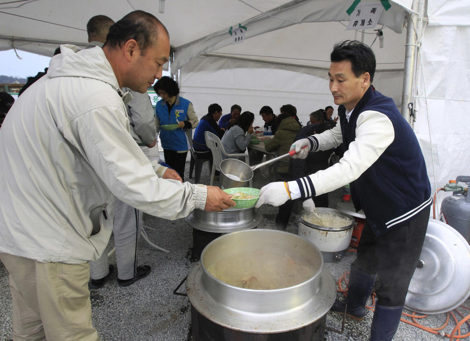 In this April 26, 2014 photo, Lim Jang-young, 58, volunteer and Japanese restaurant owner, right, ladles out a bowl of traditional beef soup to a relative of a passenger aboard the sunken ferry Sewol in Jindo, South Korea. A sense of national mourning over a tragedy that will likely result in more than 300 deaths, most of them high school students, has prompted an outpouring of volunteers. More than 16,000 people — about half the island's normal population — have come to help. (AP Photo/Ahn Young-joon)