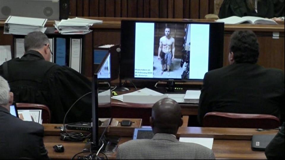 An image taken from the court pool TV via AP showing on screen a police photograph of Oscar Pistorius standing on his blood-stained prosthetic legs and wearing shorts covered in blood, taken shortly after the athlete fatally shot his girlfriend, which was shown to the court in Pretoria, at his murder trial Friday, March 14, 2014. Prosecutors displayed two photos on TV monitors in the courtroom. In one, the muscled Olympic athlete, who is shirtless, is standing facing the camera wearing his prosthetics. There are blood stains up to the knees of his limbs and his shorts are also bloodied, but his naked chest appears to be clean of blood. A second photograph shows Pistorius from the waist up and from the left side, also showing blood on his shorts and parts of his body, with a tattoo visible on his back. The photographs were taken in the garage of Pistorius’ Pretoria home where the athlete killed Reeva Steenkamp in the early hours of Valentine’s Day, 2013, a former policeman testified. (AP Photo/Court Pool via AP)