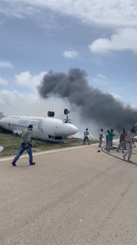 Firefighters spray water on a plane that flipped over after a crash landing, in Mogadishu