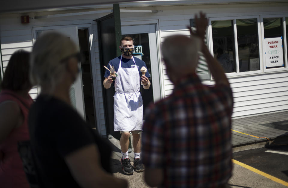 Brendan Kenny serves customers with masks at a Brickley's Ice Cream shop, one of two stores, in Narragansett, R.I., Wednesday, July 29, 2020. The other nearby location closed when teenage workers were harassed by customers who refused to wear a mask or socially distance. Disputes over masks and mask mandates are playing out at businesses, on public transportation and in public places across America and other nations. (AP Photo/David Goldman)