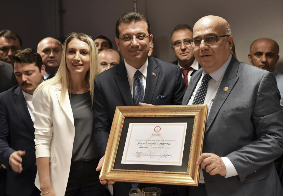 Ekrem Imamoglu, the candidate of Turkey's main opposition Republican People's Party, center, and his wife Dilek Imamoglu pose with a certificate confirming his election victory, in Istanbul, Thursday, June 27, 2019. Imamoglu is formally taking office as mayor of Istanbul four days after he won a repeat election in Turkey's largest city and commercial hub. (Imamoglu Team via AP, Pool)