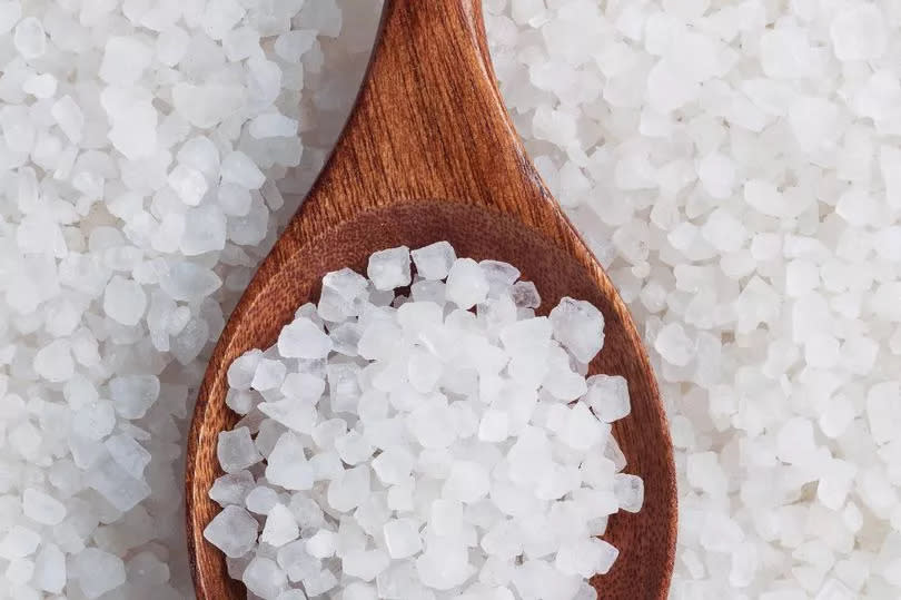 Top view of wooden spoon full of rock sea salt on salt crystal.