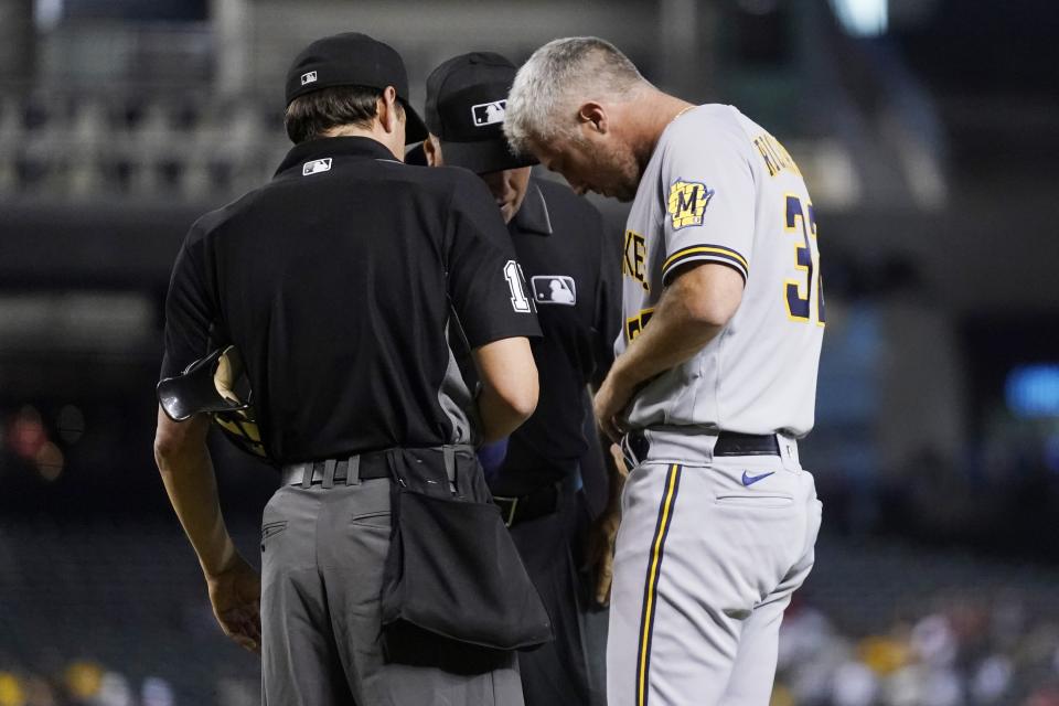 Milwaukee Brewers relief pitcher Trevor Richards, right, turns his belt around as umpires D.J. Reyburn, left, and Brian O'Nora, center, examine his belt, glove and cap during the second inning of a baseball game against the Arizona Diamondbacks, Monday, June 21, 2021, in Phoenix. Beginning Monday, Major League Baseball will enhance its enforcement of rules that prohibit applying foreign substances to baseballs. (AP Photo/Ross D. Franklin)