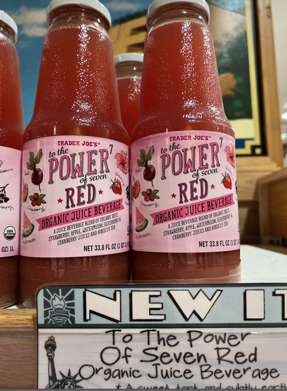 Sign and bottles labeled "Trader Joe's Organic Red Juice" on a shelf, with "NEW" and description below