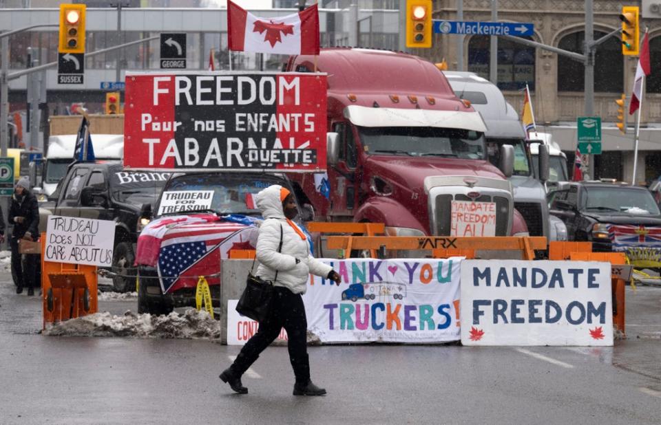 A woman crosses the street in front of vehicles parked as part of the trucker protest,  Tuesday, Feb. 8, 2022 in Ottawa. (Adrian Wyld /The Canadian Press via AP)