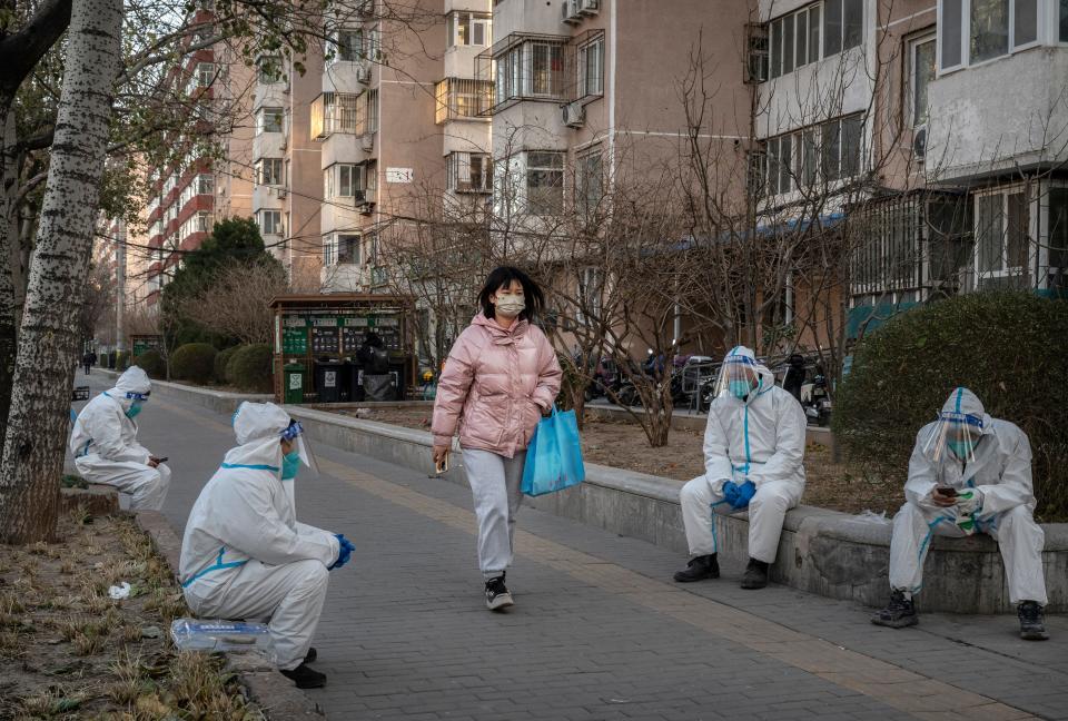 A pedestrian walks by epidemic control workers who work in sanitation wearing PPE to protect against the spread of COVID-19 as they wait to remove medical waste taken from apartments where people who have tested positive are doing home quarantine on December 6, 2022 in Beijing, China.