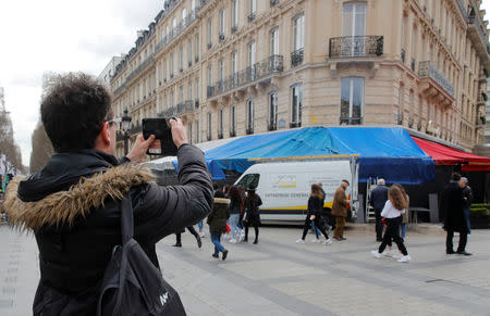 A man takes pictures of the Fouquet's restaurant burned during the last "yellow vests" protest on the Champs Elysees avenue in Paris, France, March 18, 2019. REUTERS/Philippe Wojazer