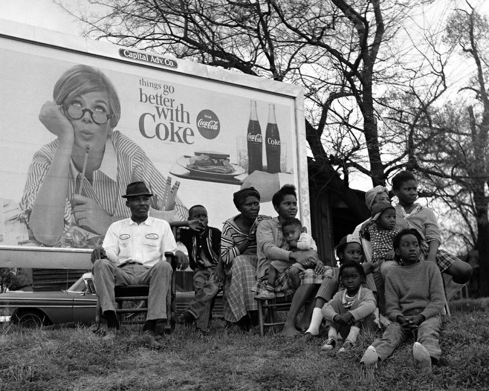 "Things Go Better With Coke" sign and multi-generational family watching marchers, 1965.