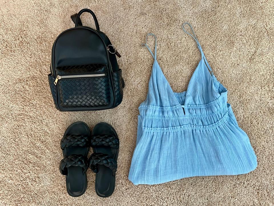 Black backpack, black sandals, baby blue dress spread out on floor.