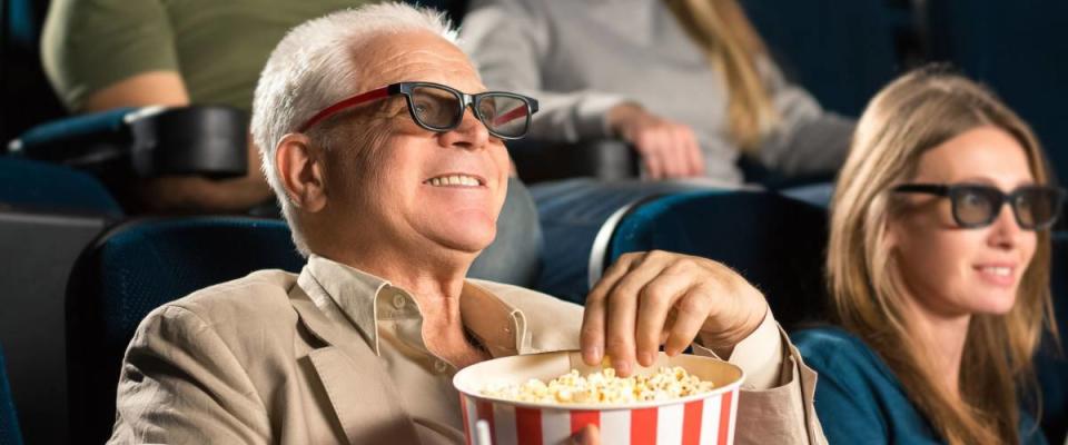 Good old movies. Cheerful senior man wearing 3D glasses grabbing popcorn while enjoying a movie with his family at the cinema copyspace seniority happiness industry fun leisure concept