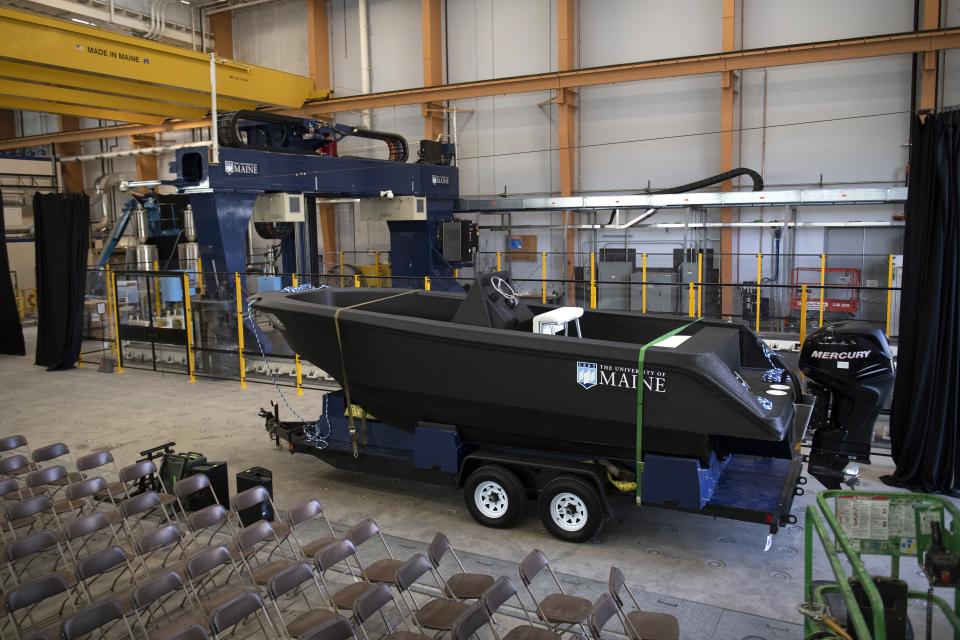 A 25-foot, 5,000-pound patrol boat that was produced using a large polymer 3D printer, behind left, rests on a trailer on the campus of the University of Maine. The boat was printed at the school’s Composites Center on the world’s largest polymer 3D printer.