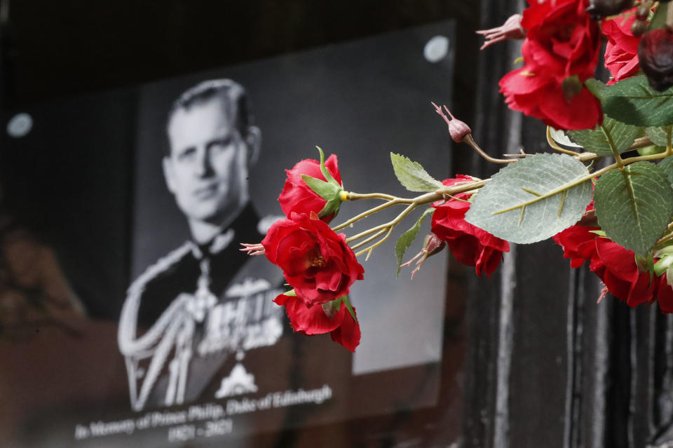 Flowers in front of a photograph of Britain's Prince Philip outside Windsor Castle in Windsor, England after the announcement regarding the death of Britain's Prince Philip, Friday, April 9, 2021. Buckingham Palace officials say Prince Philip, the husband of Queen Elizabeth II, has died. He was 99. Philip spent a month in hospital earlier this year before being released on March 16 to return to Windsor Castle. (AP Photo/Frank Augstein)