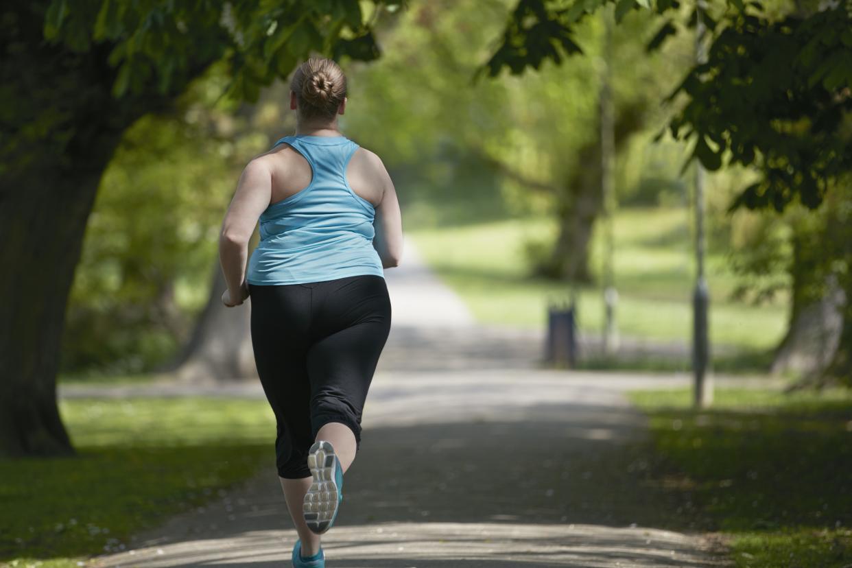 A young woman, seen from behind, runs along a tree-lined path.